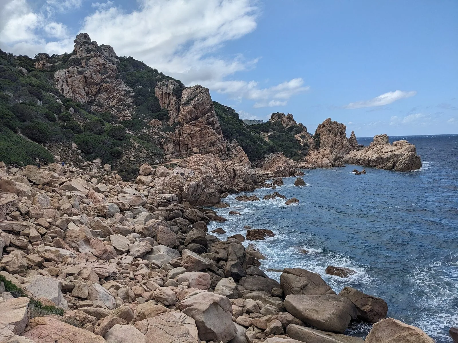 Scogliere e massi di granito rosato lungo la costa di Costa Paradiso, sul sentiero verso Li Cossi, con il mare blu a destra
